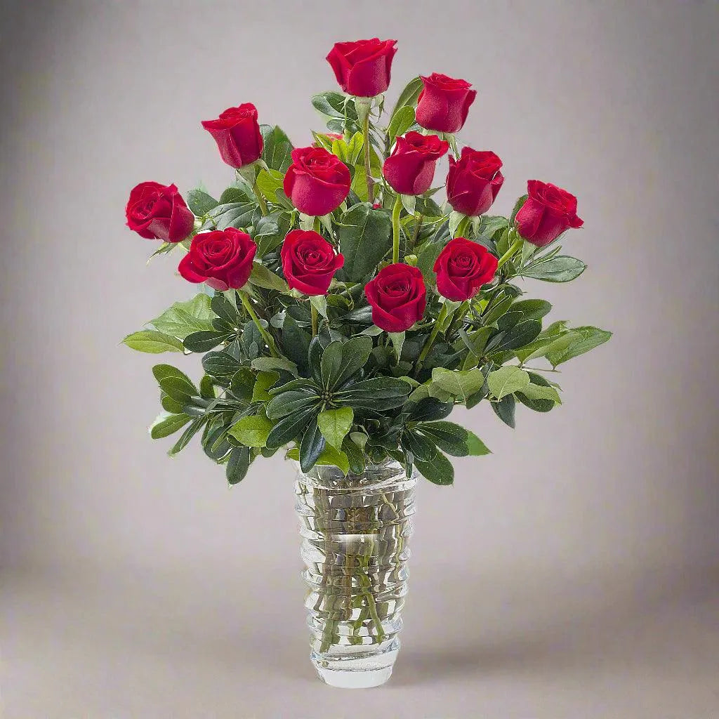 A beautiful arrangement of a dozen long-stemmed roses in a clear glass vase.