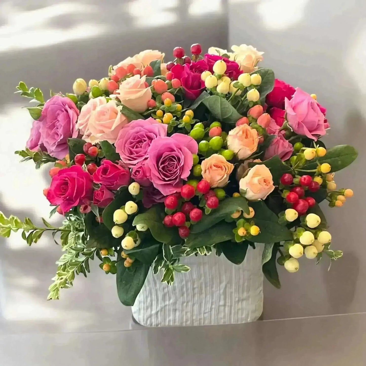 Bright mixed flower bouquet with pink roses and colorful berries in white vase, vibrant and uplifting
