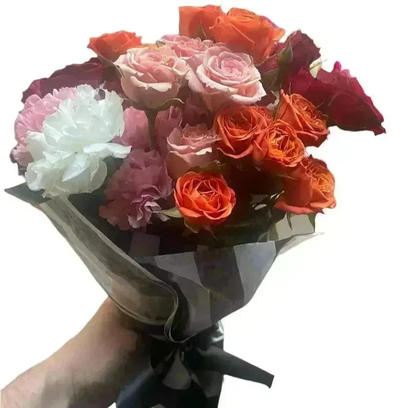 Hand-tied bouquet with vibrant orange roses, soft pink roses, and white carnations in black wrapping