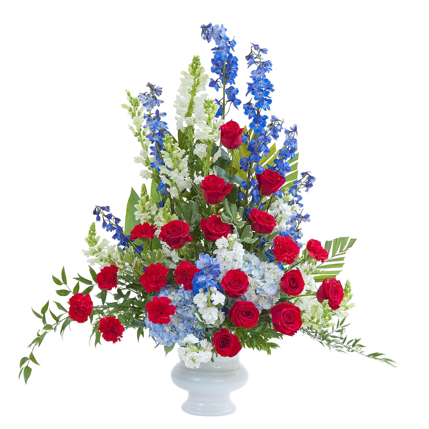 Uplifting patriotic flower arrangement with red roses, blue delphiniums, white snapdragons, and greenery in white vase