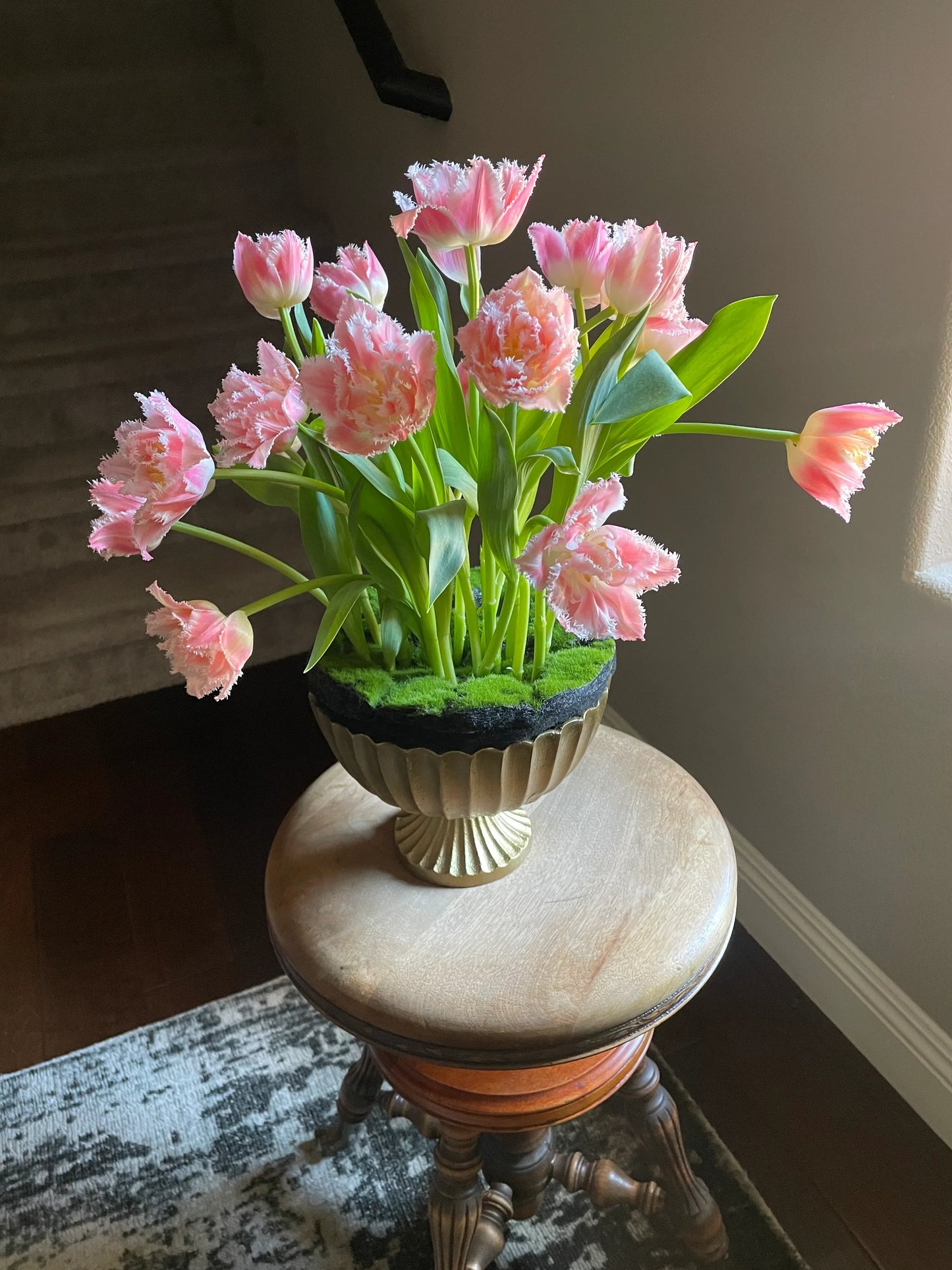 A uniquely modern arrangement of tulips in an urn appearing as if they grew up through the moss and dirt.