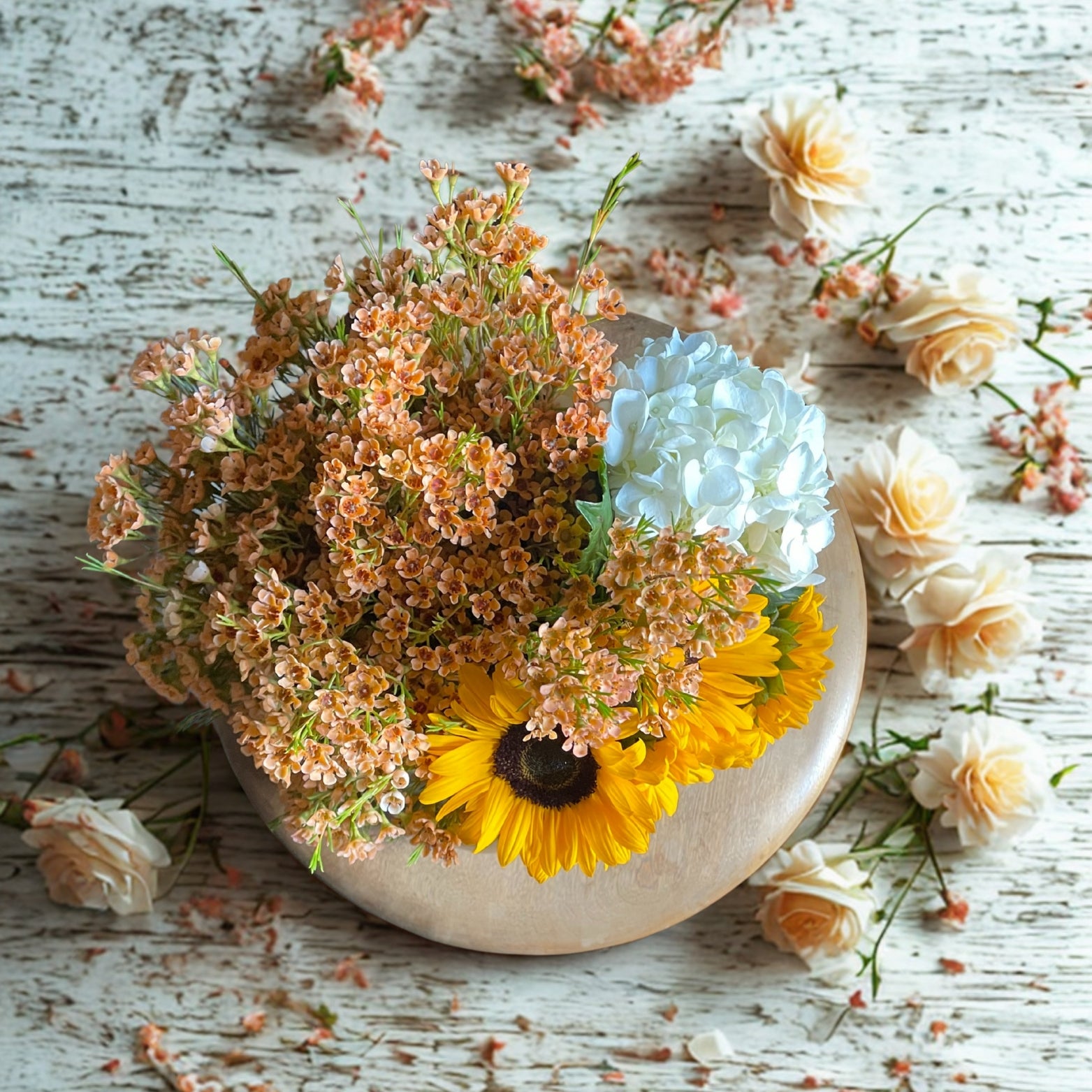 An aerial view of a flower arrangement in a golden pumpkin with mini sunflowers, blue hydrangea, and orange wax flowers.