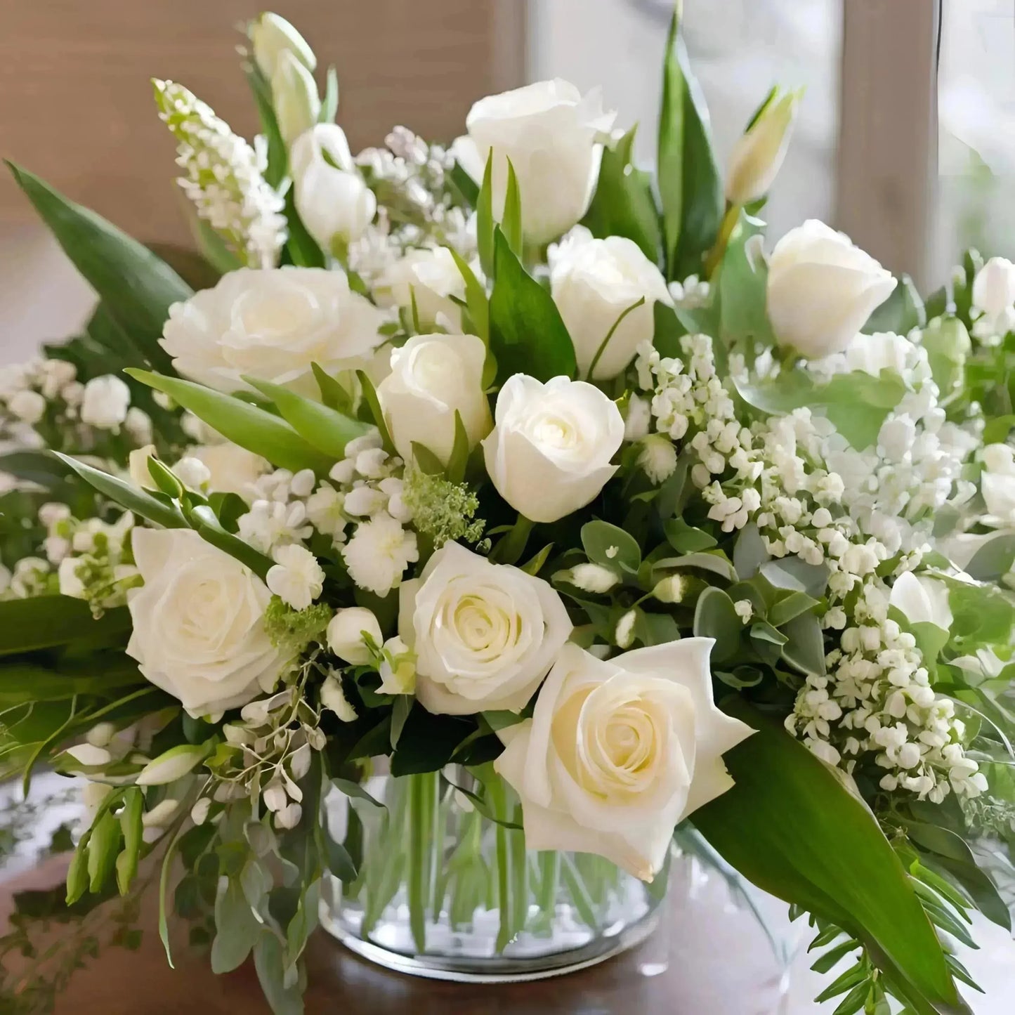 Uplifting sympathy arrangement with white roses and lush greenery in glass vase