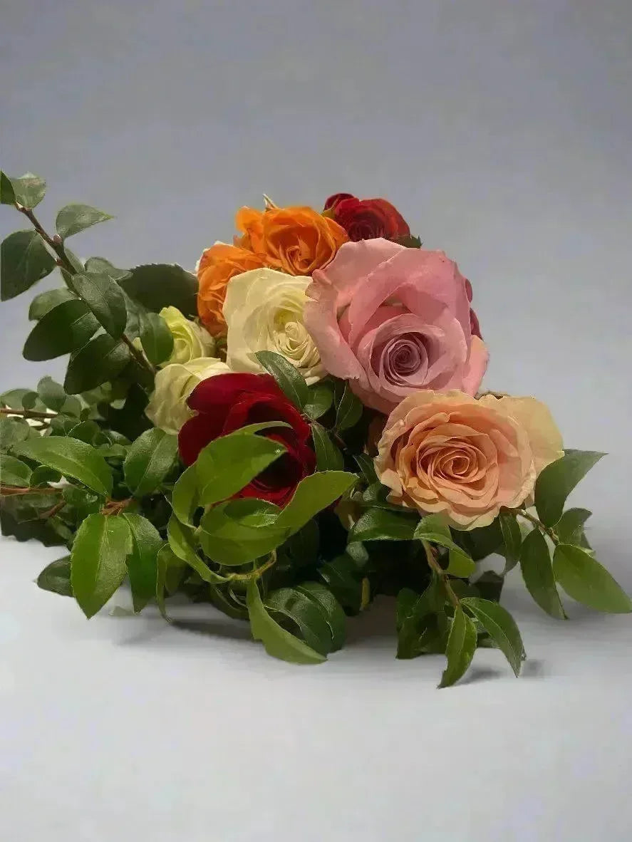 Uplifting hand-tied bouquet of vibrant pink, red, orange, and cream roses with lush green leaves