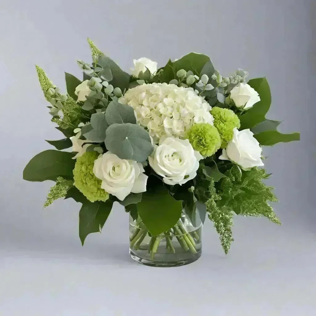 Elegant sympathy flower arrangement with white roses, green blossoms, eucalyptus, and lush foliage in glass vase