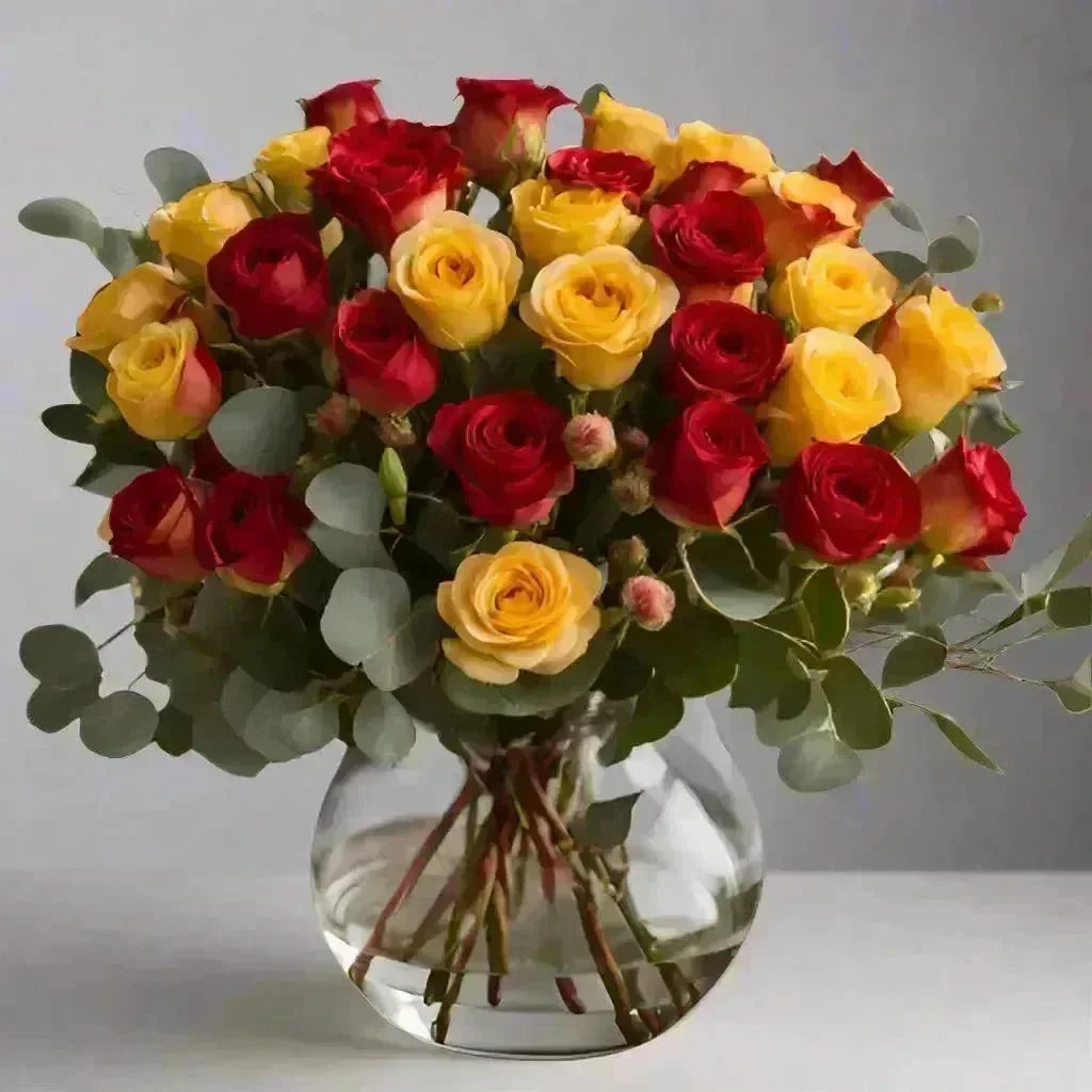 Bright red and yellow roses bouquet with eucalyptus in clear glass vase, uplifting floral arrangement