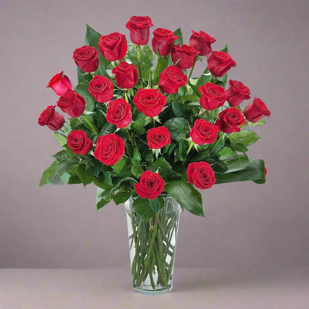 Two dozen beautiful red roses in a glass vase with Saalal and other seasonal greenery.
