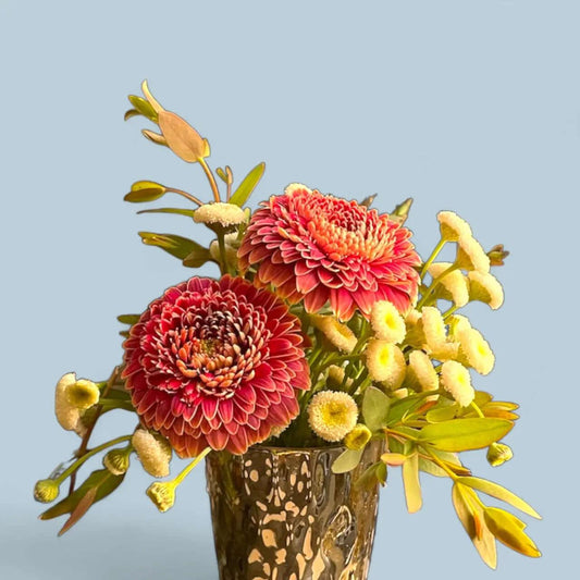 Bright bouquet with vibrant red dahlias and small yellow flowers in decorative glass vase on blue