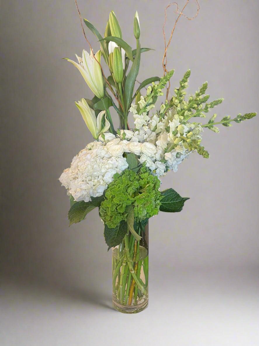 Elegant bouquet of fresh white lilies, hydrangeas, and green foliage in clear glass vase