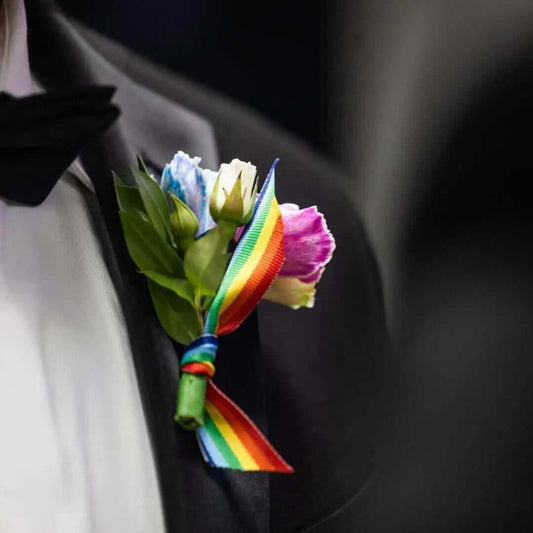 Close-up of a boutonniere with colorful flowers and a vibrant rainbow ribbon on a black tuxedo jacket