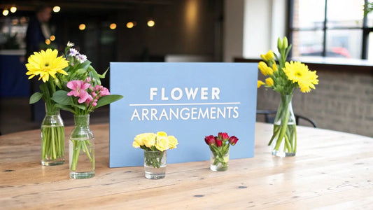 Bright flower arrangements in vases on wooden table with cheerful blue 'Flower Arrangements' sign