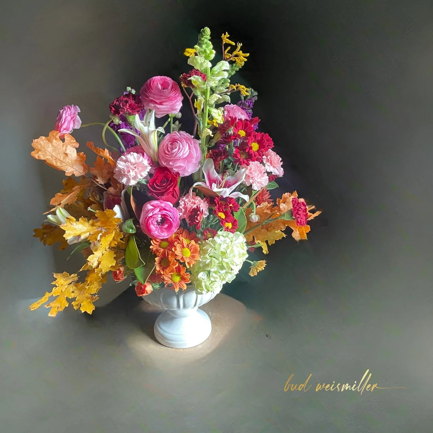 Bright and uplifting floral arrangement with pink roses, lilies, carnations, and autumn leaves in white vase