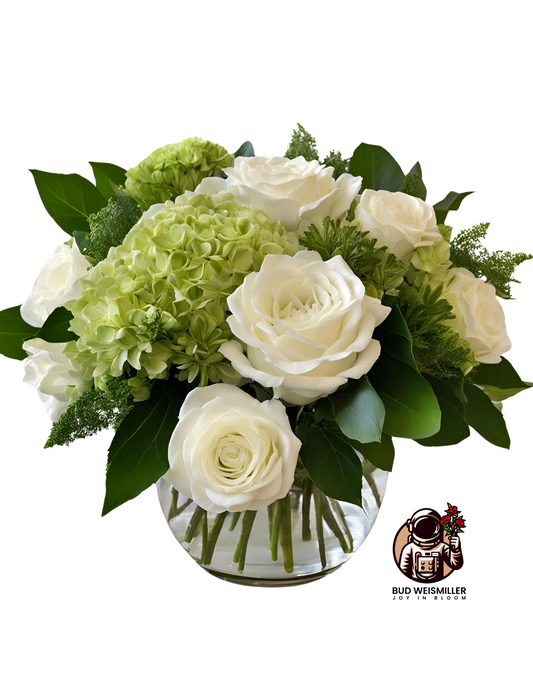 A premium size sympathy arrangement with large white roses, white and green hydrangea, green button ponpoms, and lush greenery in a clear, up-cycled vase.