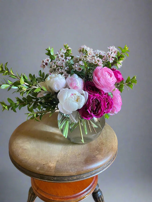 Bouquet of flowers in a clear vase on a wooden stool with a gray background.