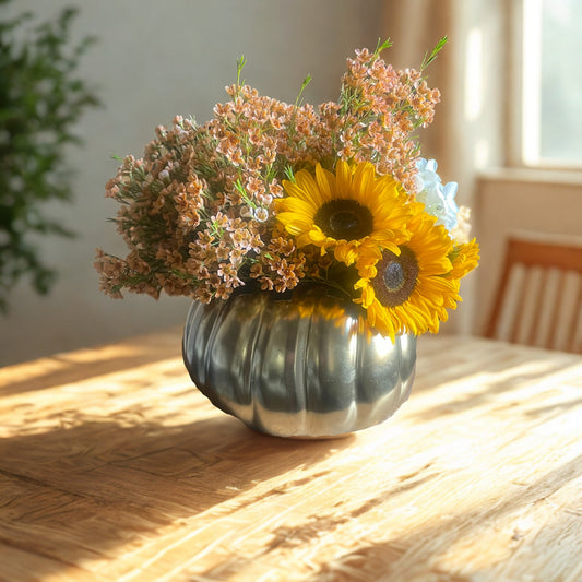 A golden pumpkin vase filled with mini sunflowers, blue hydrangea, and orange wax flower.