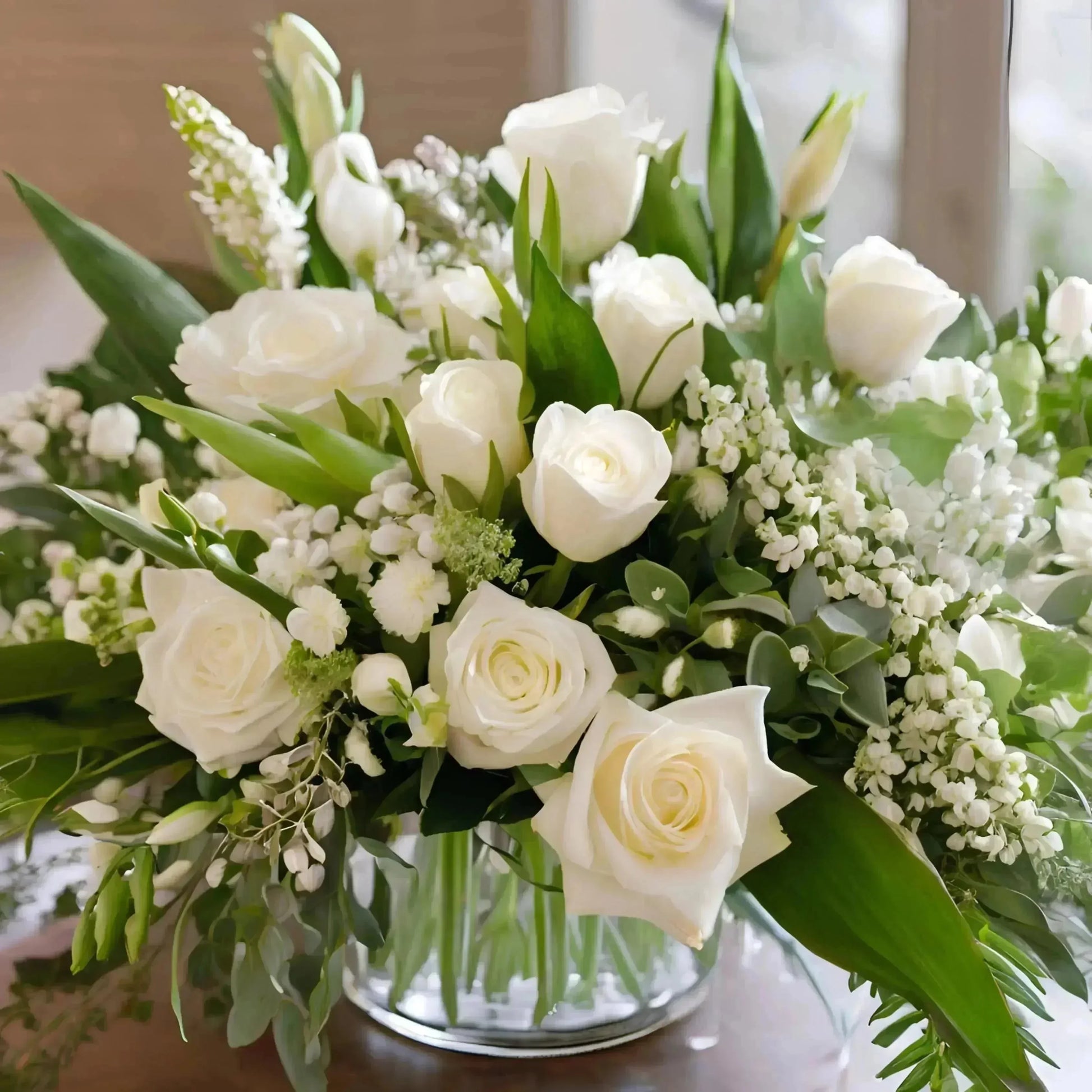 Bouquet of white roses and greenery in a clear vase.