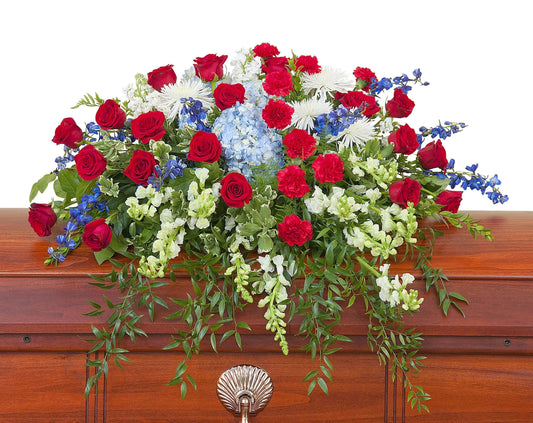 Floral arrangement with red, white, and blue flowers on a wooden casket.
