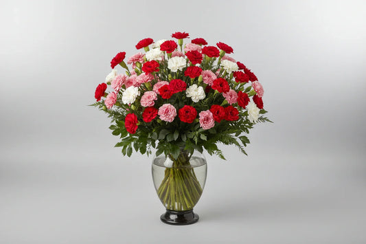 Bouquet of red, pink, and white carnations in a clear vase on a marble surface.