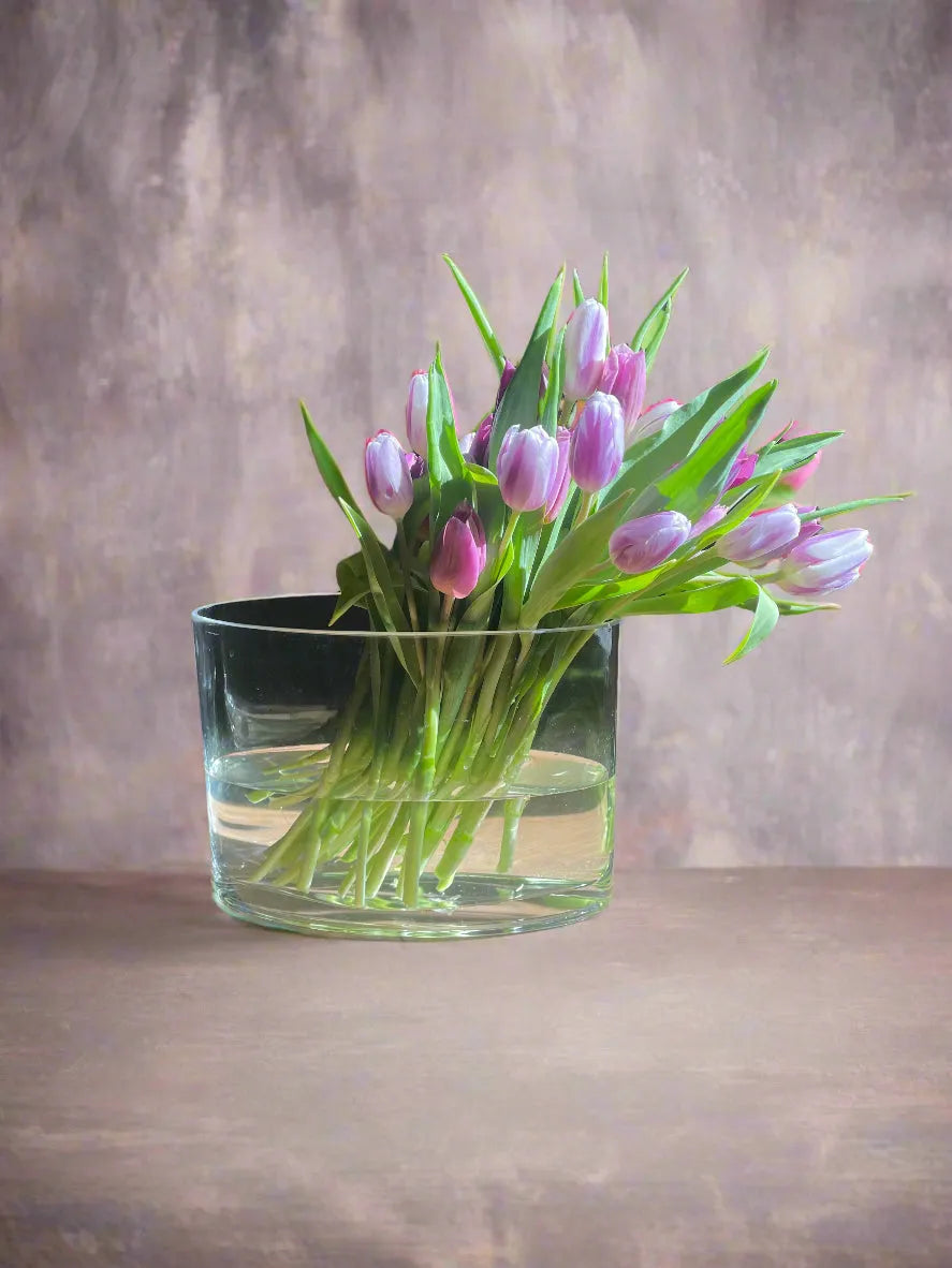 A beautiful bouquet of tulips arrangement in a modern style in a clear glass oval vase.