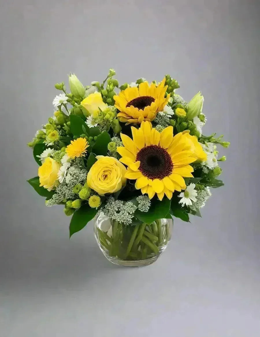 Bouquet of sunflowers and yellow roses in a clear vase on a gray background