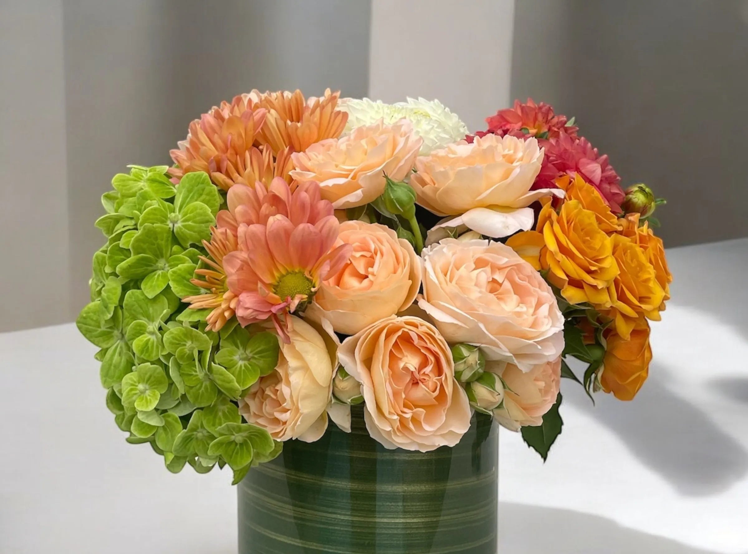 A beautiful flower arrangement featuring shamrock hydrangea, salmon mums, and peach spray roses in a glass vase lined with banana leaf.